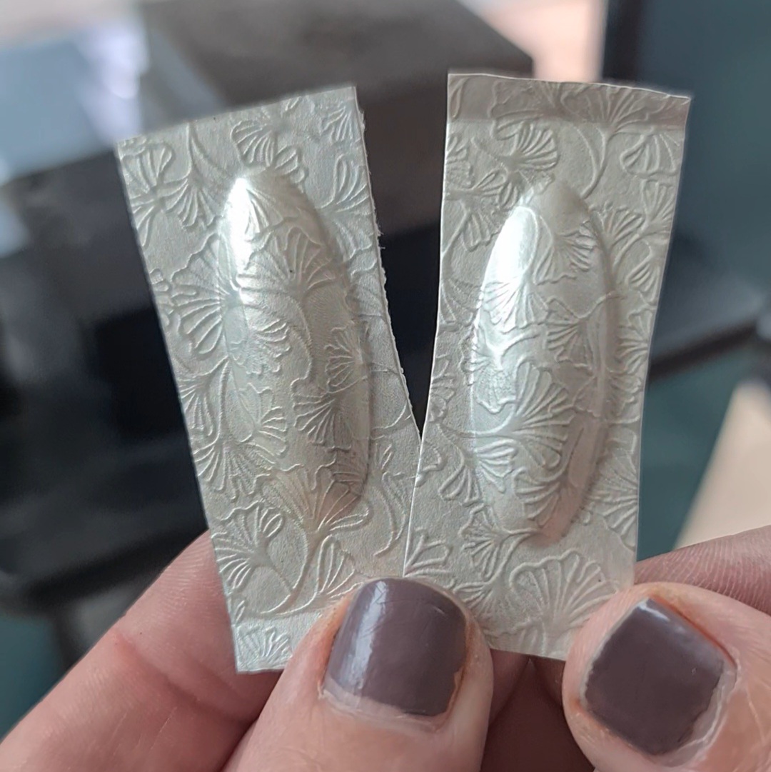 image shows two pieces of silver sheet, each with a puffed oval shape in the middle